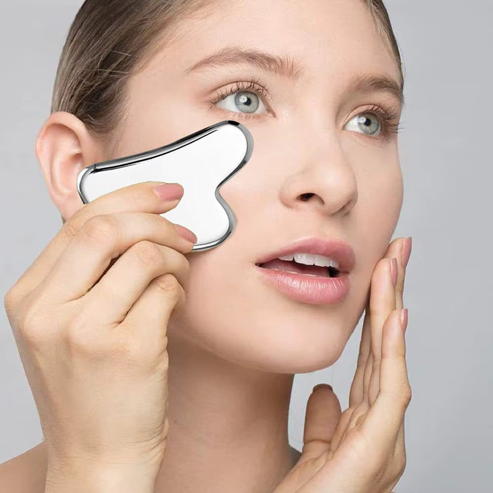 Woman performing self-massage using SkinSculpt™ stainless steel Gua Sha tool for facial relaxation and skin rejuvenation